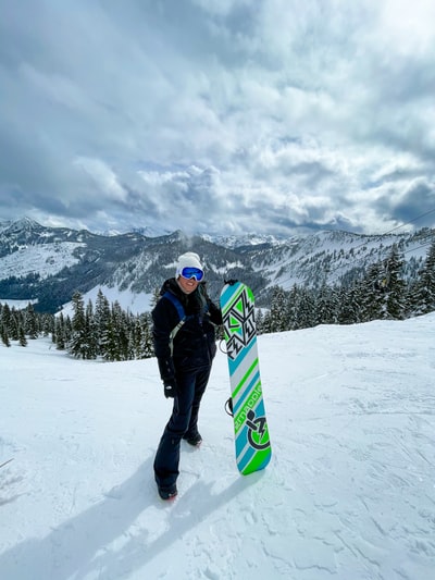 身穿黑色夹克和蓝色裤子的男子在积雪覆盖的地面上手持绿色和黄色的滑雪板